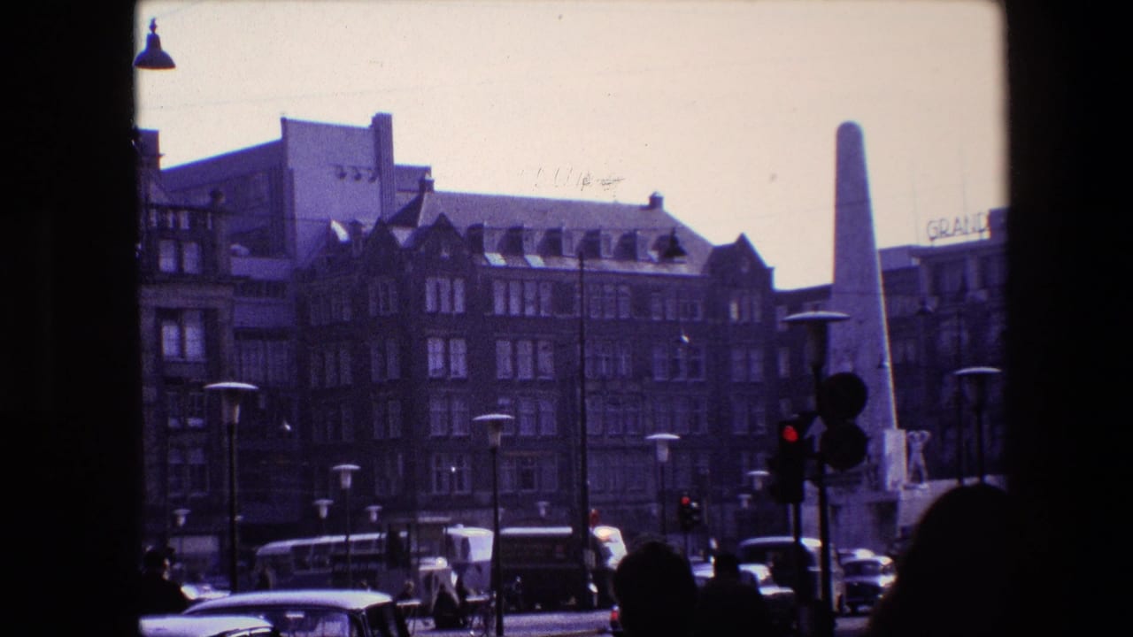 Amsterdam intersection scene with the monument centered near traffic signals, pedestrians in silhouette, period cars, street lamps, and a partial building sign.