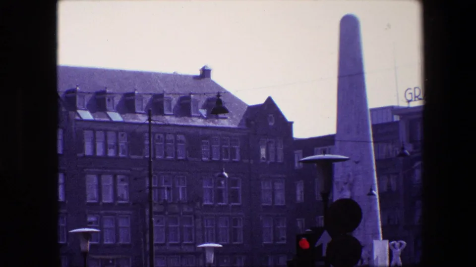 1967 Amsterdam street view with a pale obelisk, brick hotel-like facade, rooftop GRAND lettering, lamps, and traffic signal silhouettes.