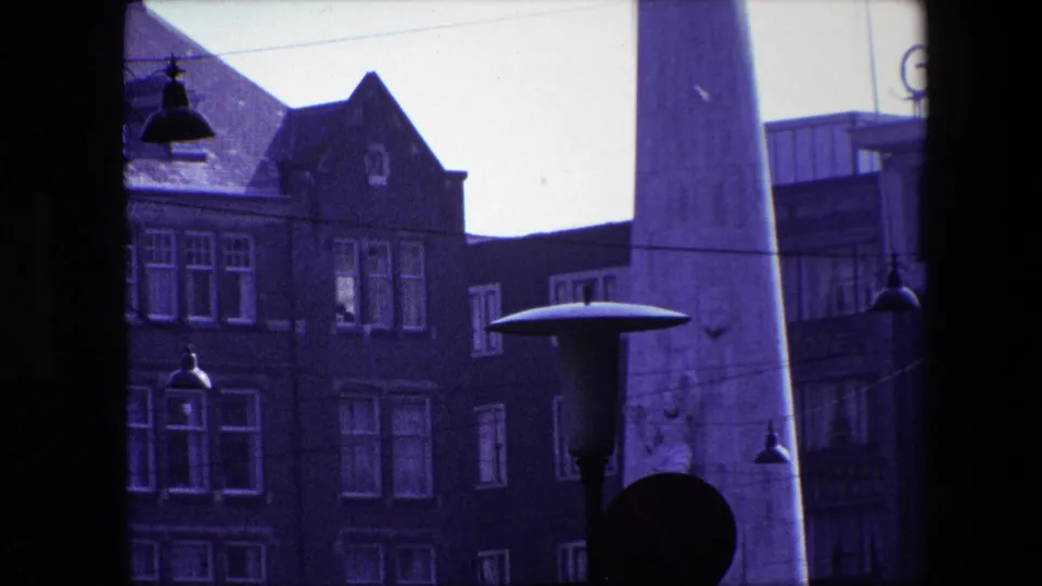 Closer 1967 Amsterdam street view with gabled brick architecture, a cropped obelisk, window rows, a broad street lamp, and dark traffic signal silhouettes.