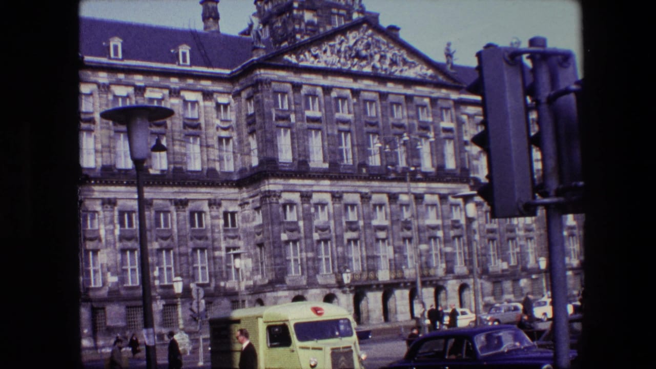1967 Amsterdam home-movie frame showing the Royal Palace on Dam Square with a yellow delivery van, classic cars, pedestrians, and street fixtures below the stone facade.