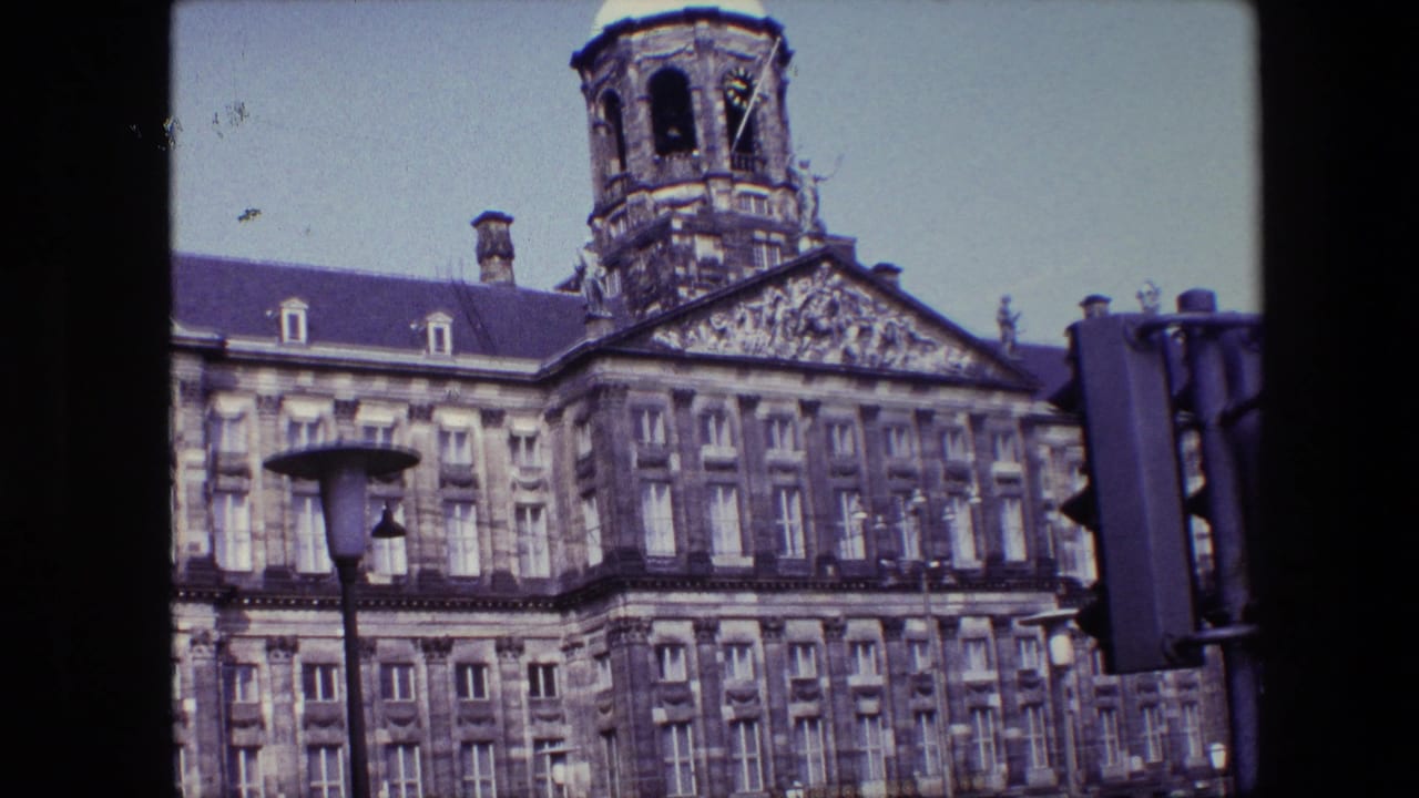 1967 8mm frame of the Royal Palace of Amsterdam facade with its tower above the roofline, a street lamp in front, and a traffic signal at the right edge.
