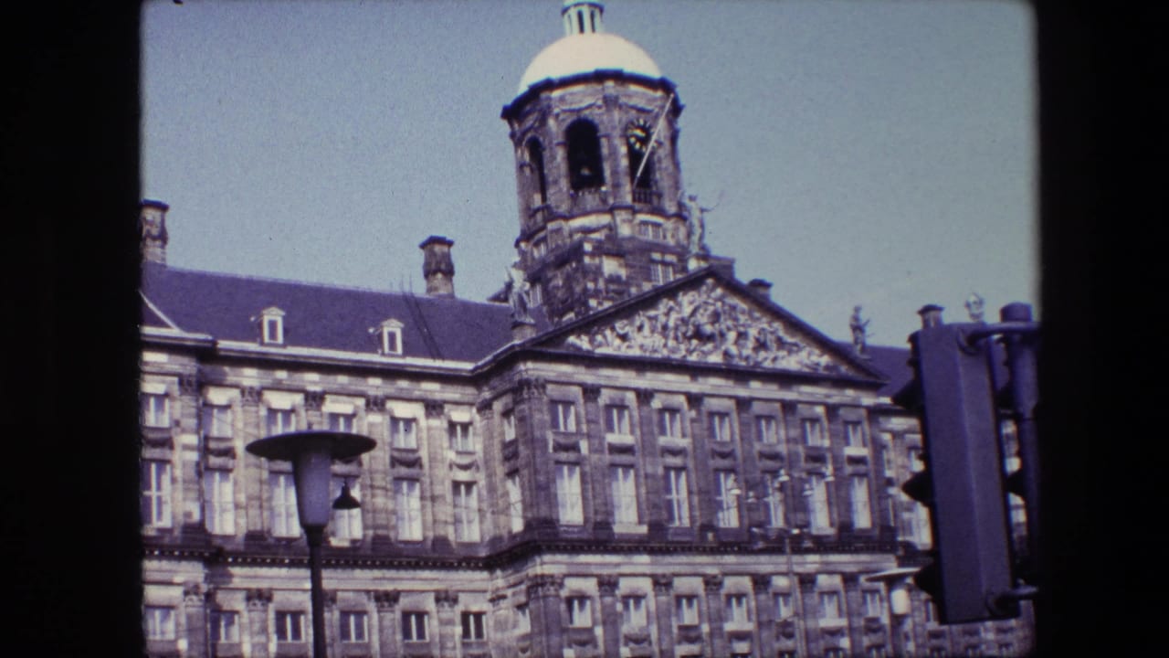 1967 8mm frame showing the Royal Palace of Amsterdam tower and sculpted facade, with a street lamp and traffic signal in the foreground.