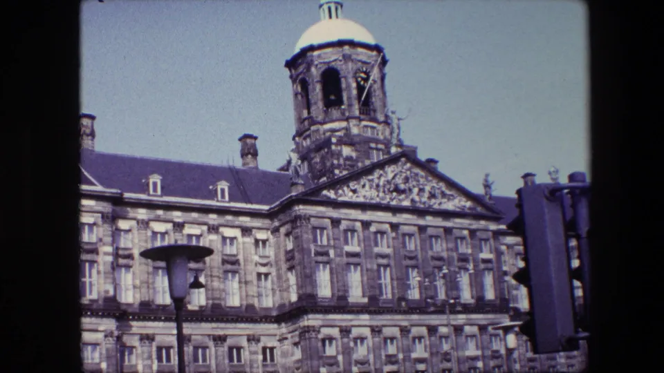 1967 8mm frame showing the Royal Palace of Amsterdam tower and sculpted facade, with a street lamp and traffic signal in the foreground.