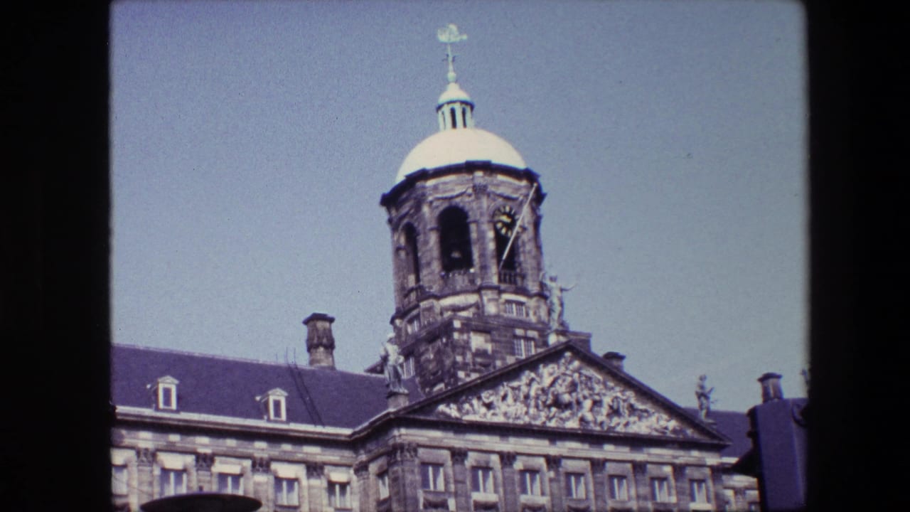 1967 archival home-movie frame of an Amsterdam domed clock tower with a sculpted pediment and roofline visible below.