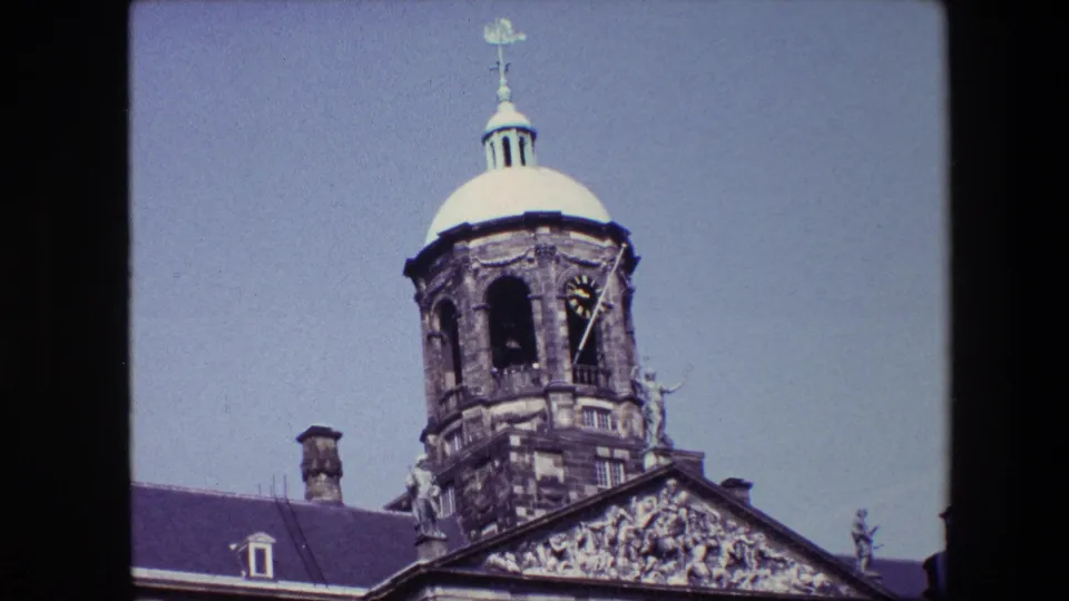 1967 Amsterdam home-movie view tightening on the domed clock tower, clock face, arched opening, and carved facade details.