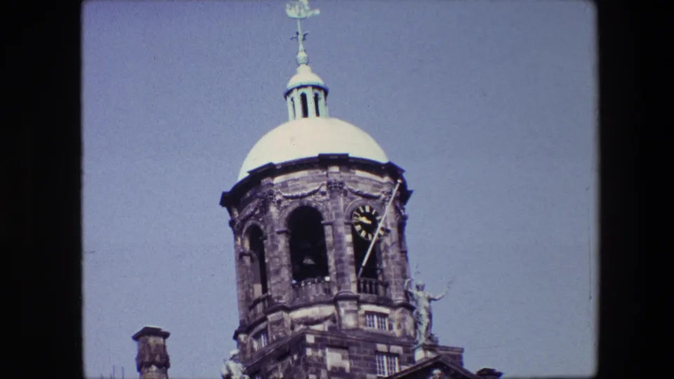 Closer 1967 archival frame of the Amsterdam domed tower, showing the clock face, dark arched opening, cupola, and stone ornament.
