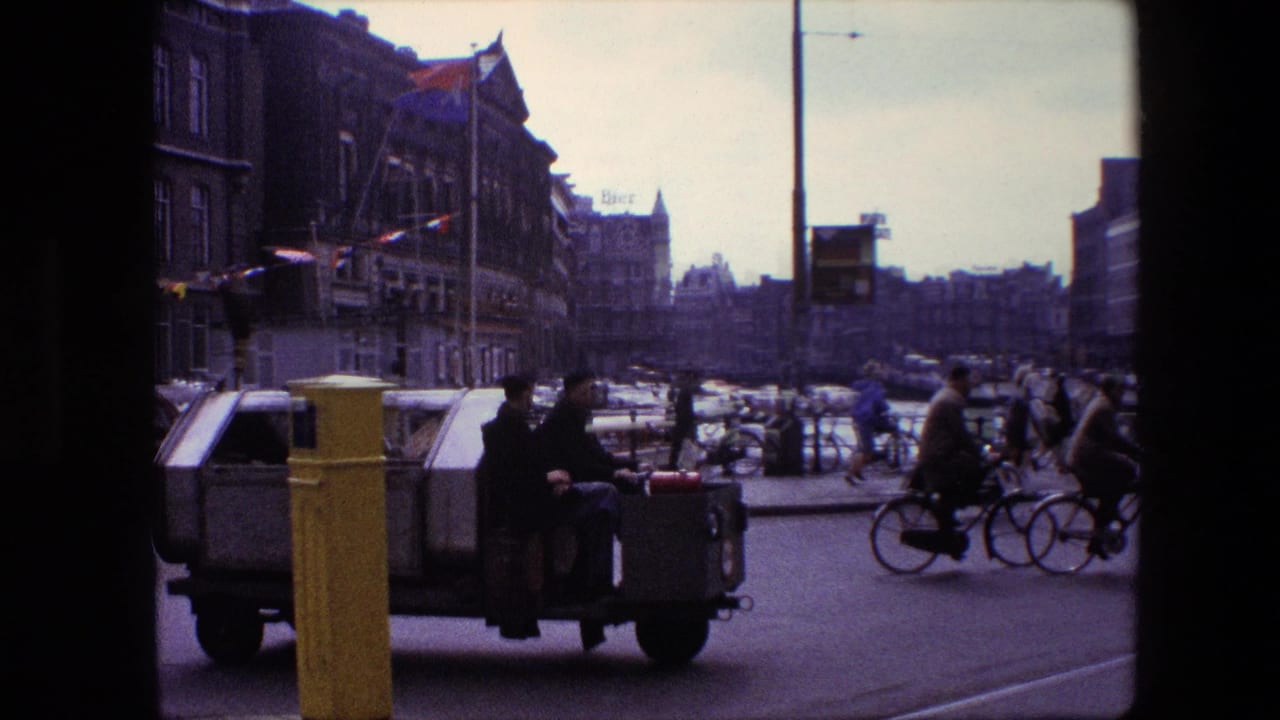 1967 Amsterdam street view with a small makeshift utility vehicle, cyclists, pedestrians, cars, gabled buildings, and a yellow post in the foreground.