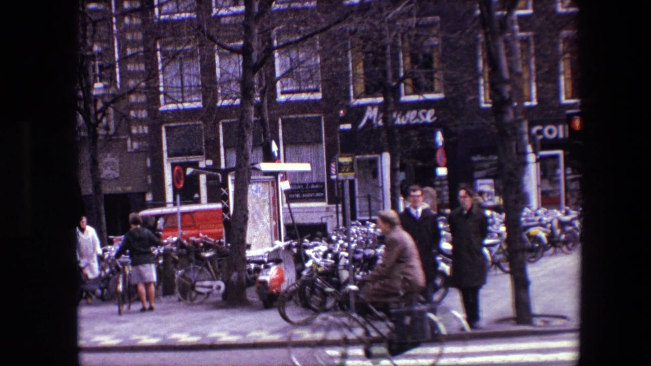1967 Amsterdam street view with pedestrians, cyclists, parked bicycles, shopfronts, bare trees, and a red van in the background.