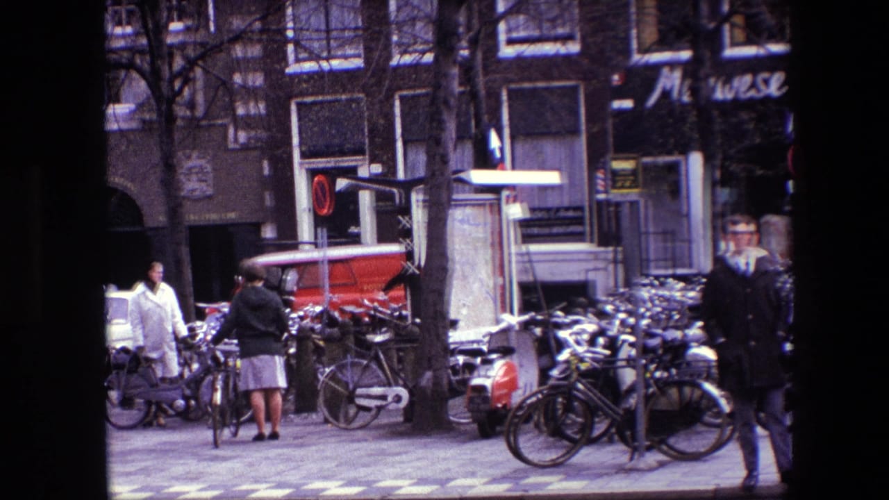 People stand and walk beside a row of parked bicycles and a red van.