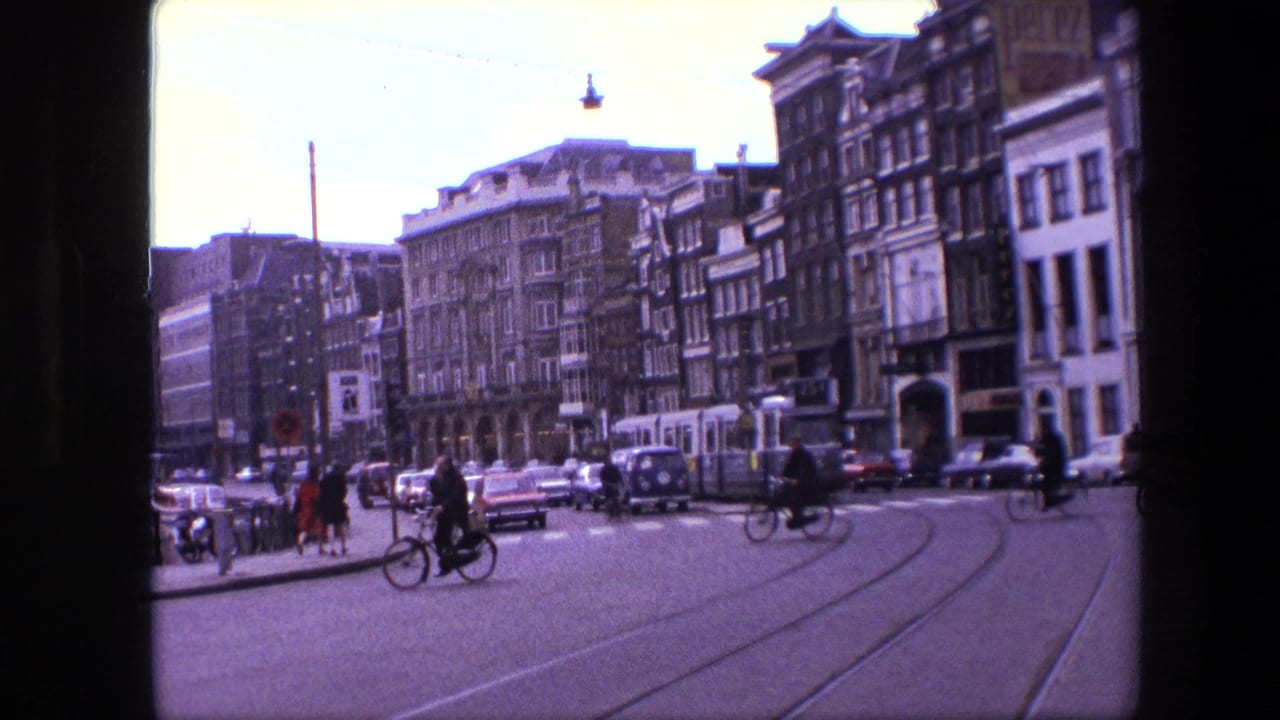 Bicyclists cross a broad street with tram tracks and stopped cars beside tall buildings.