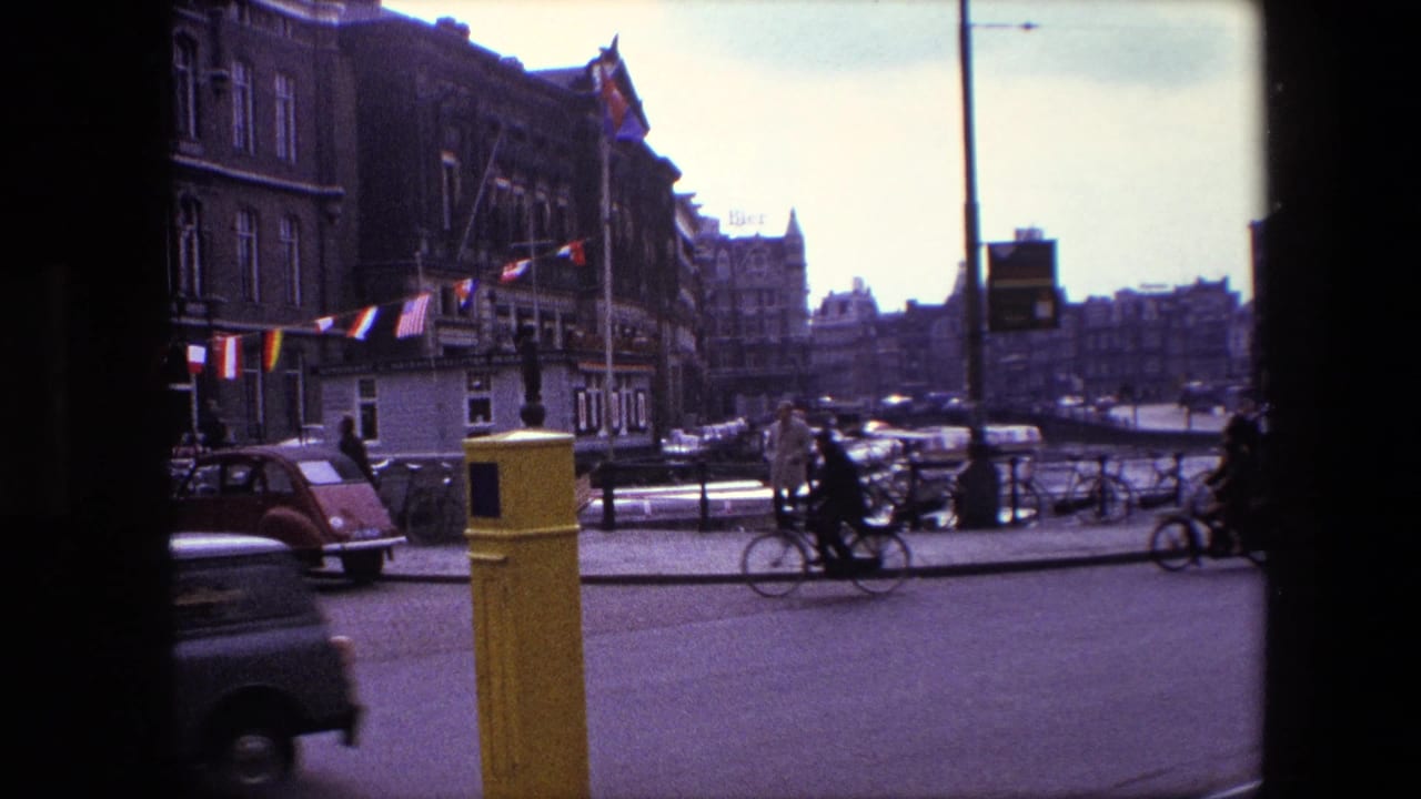 Street scene with a small car, cyclists, flags, pedestrians, and historic buildings.