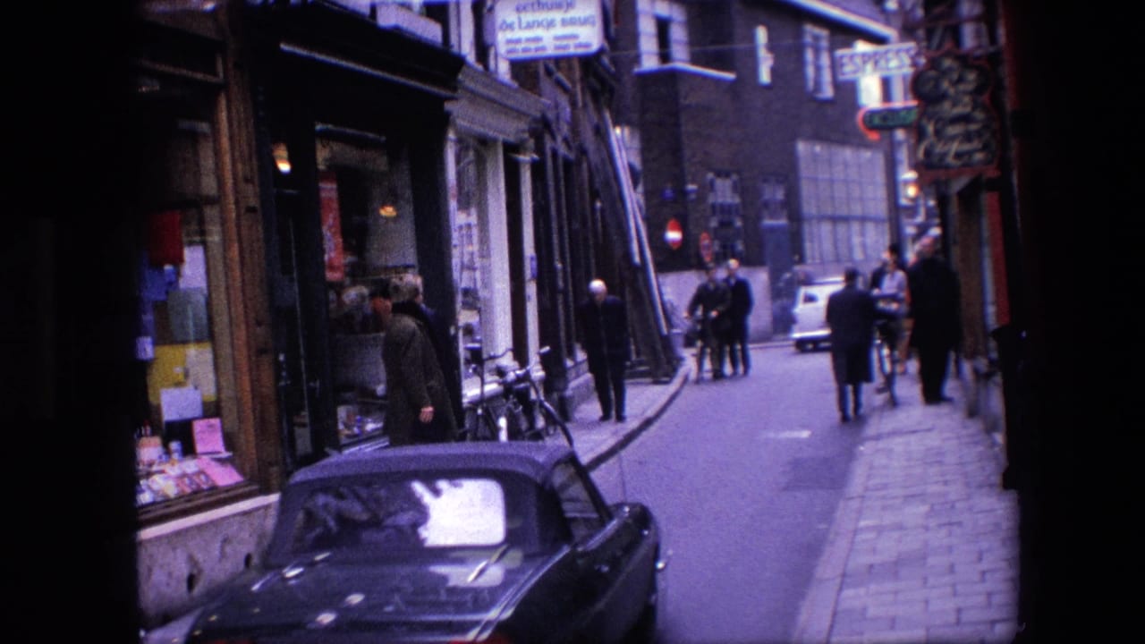 1967 Amsterdam street scene with a black convertible near shopfronts, pedestrians on the sidewalk, bicycles by the curb, and brick buildings beyond.