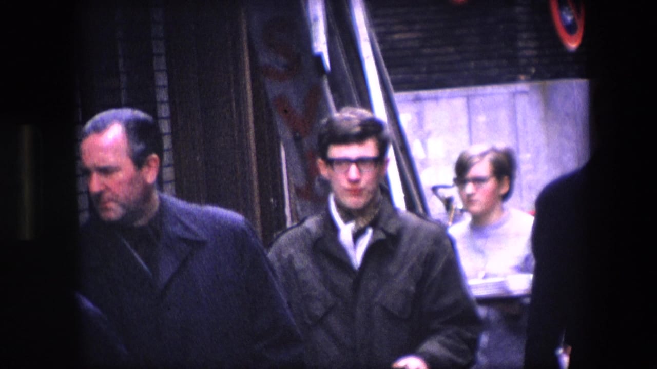 Formally dressed men, including one wearing glasses, move through a busy urban sidewalk scene in footage identified as 1967 Amsterdam.