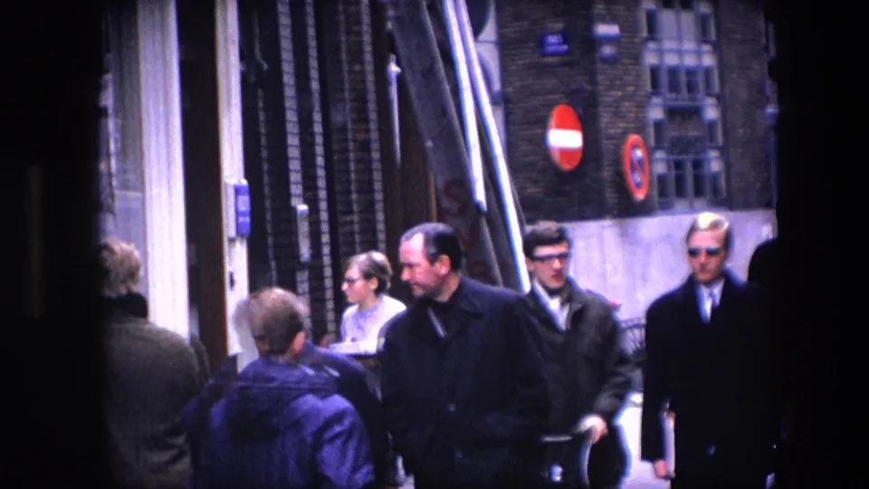 The wider street view shows men in coats, passersby, shopfronts, and circular traffic signs in a 1960s city scene identified by metadata as Amsterdam.