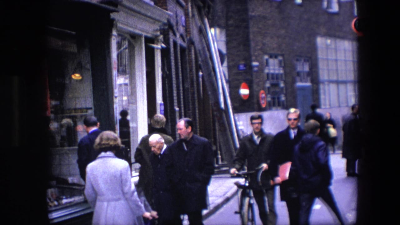 A wider handheld frame captures pedestrians moving past storefront windows, a bicycle, and street signs in footage identified as Amsterdam in 1967.