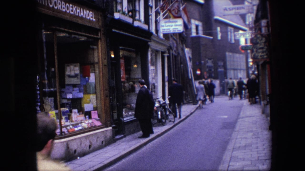 Amsterdam street scene with a bookshop display at left, a man standing near the storefront, bicycles by the curb, and pedestrians receding into the lane.