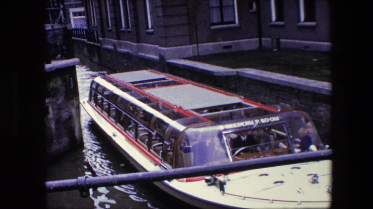 Close view of a glass-roofed canal tour boat carrying passengers beside an Amsterdam canal wall and building facade.