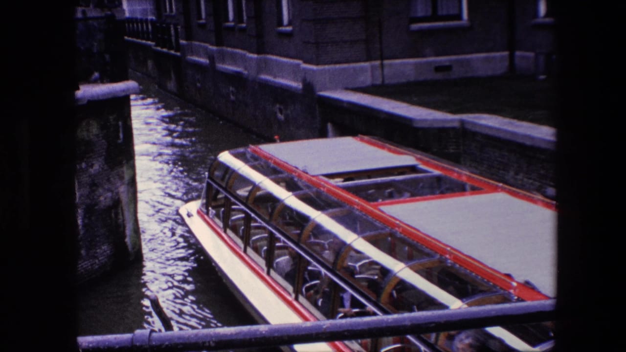 The Amsterdam sightseeing boat continues along the canal, framed by a dark vertical obstruction and masonry buildings along the water.