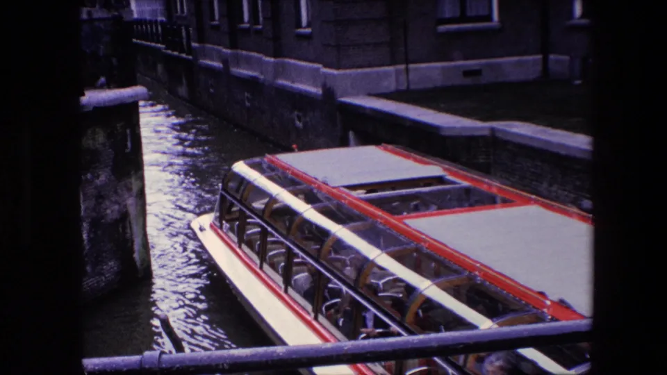 The Amsterdam sightseeing boat continues along the canal, framed by a dark vertical obstruction and masonry buildings along the water.