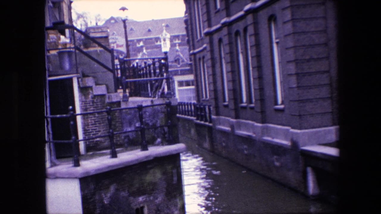 1967 Amsterdam canal view showing a confined waterway between masonry buildings, with stone canal edges, black railings, steps, and reflective water below.