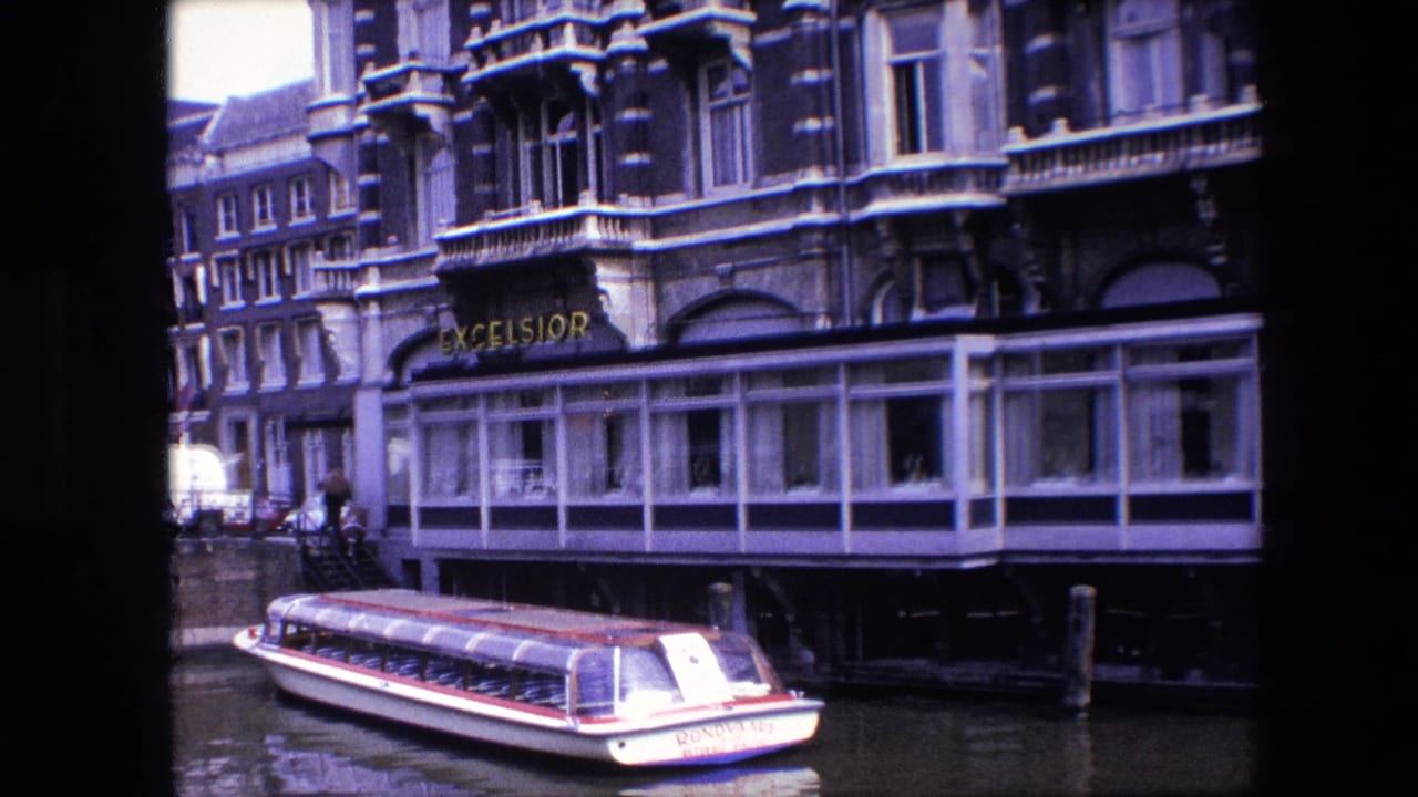 1967 Amsterdam canal view with a red-and-white covered tourist boat passing below the Excelsior hotel facade and large waterfront windows.