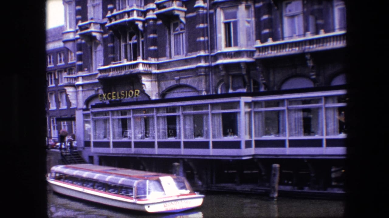 Tour boat moving along a canal in front of an ornate building marked Excelsior.