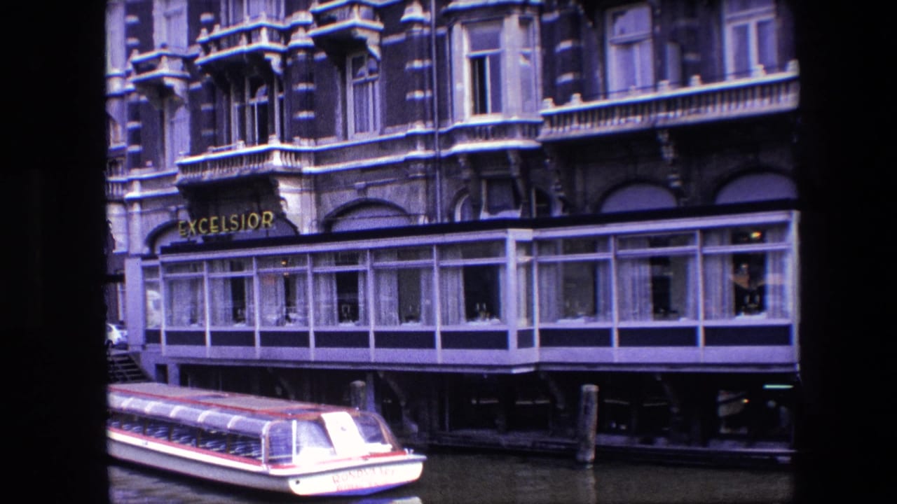 1967 Amsterdam visitor-shot frame of the Excelsior hotel frontage over the canal, with the red-and-white tour boat partly exiting the lower portion of the frame.