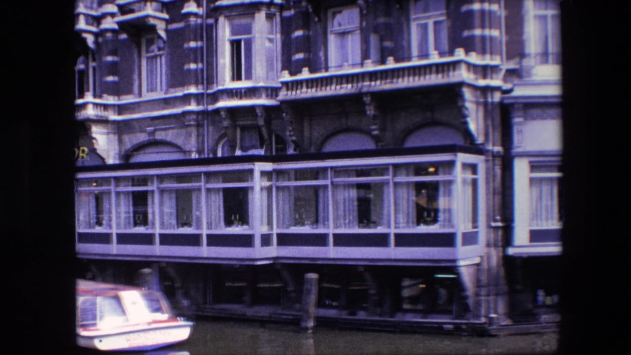 Amsterdam canal-side facade in 1967, showing the glass-enclosed lower level, dark awnings, mooring posts, and the edge of a small boat at left.