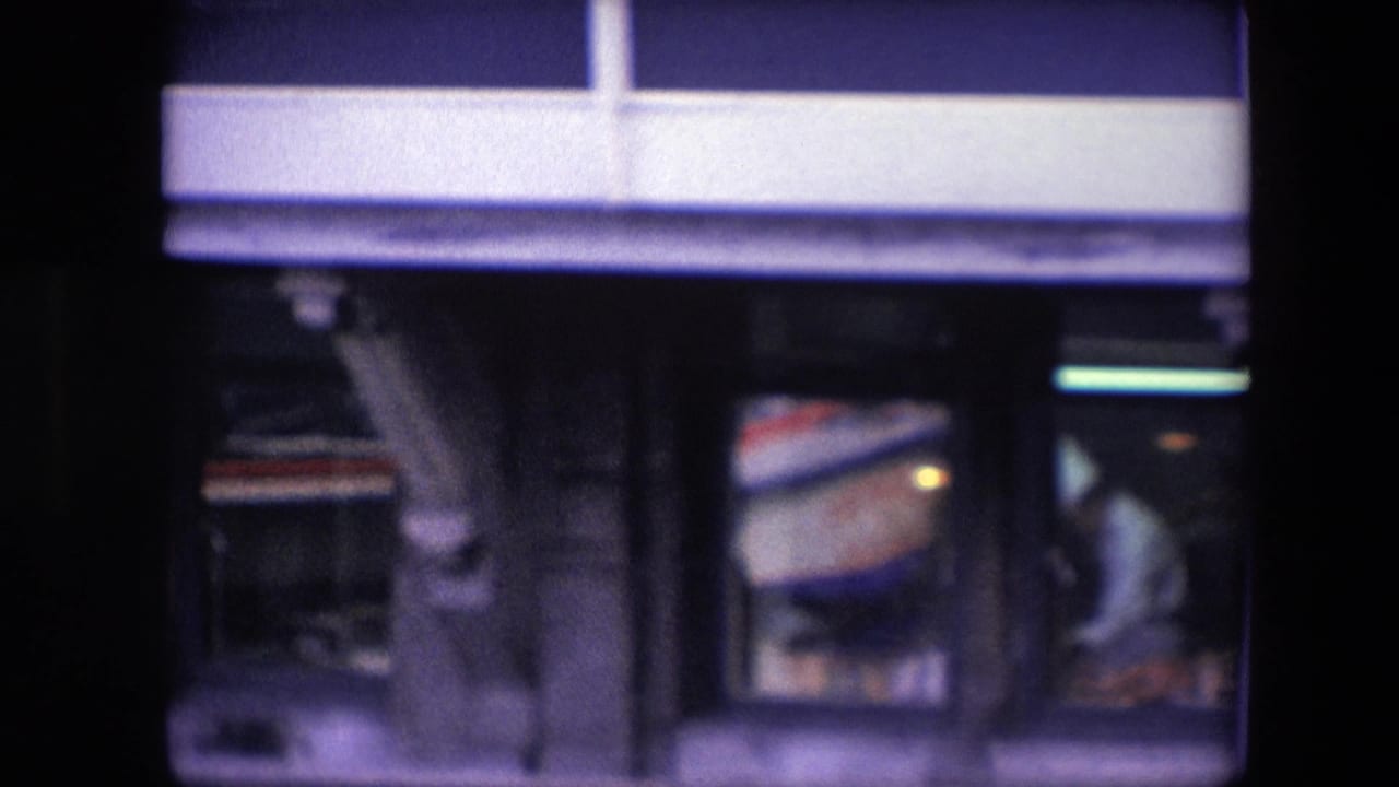 Tight archival frame of the restaurant-level windows, showing a white-uniformed chef-like figure working inside beneath the blue-and-white waterfront facade.