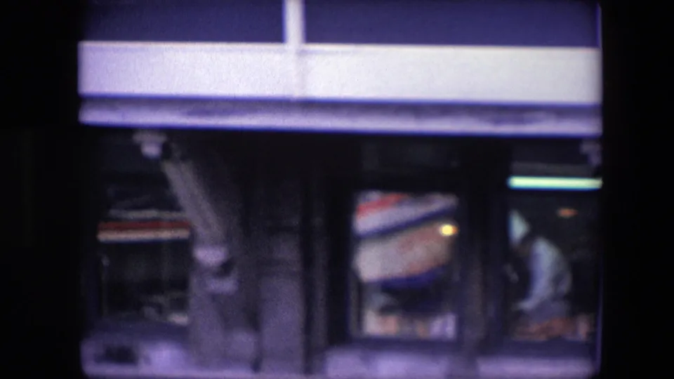 Tight archival frame of the restaurant-level windows, showing a white-uniformed chef-like figure working inside beneath the blue-and-white waterfront facade.