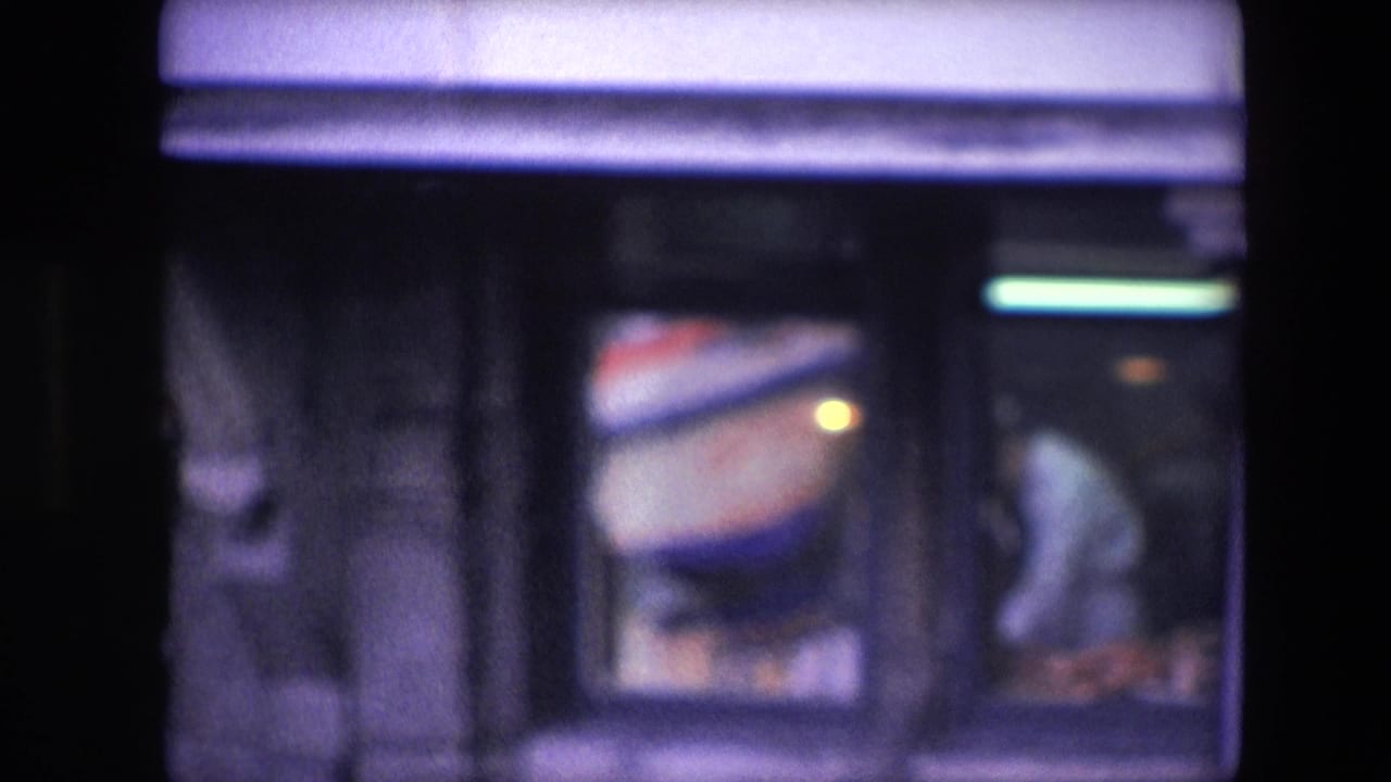 Amsterdam 1967 8mm frame showing a dim Chinese restaurant interior through glass, with a man in a light shirt bent over a preparation area.