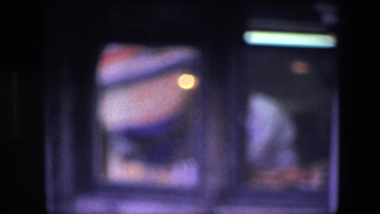 Soft-focused 1967 restaurant window view in Amsterdam, with a man partly visible at right and bright interior lighting reflected near the top.