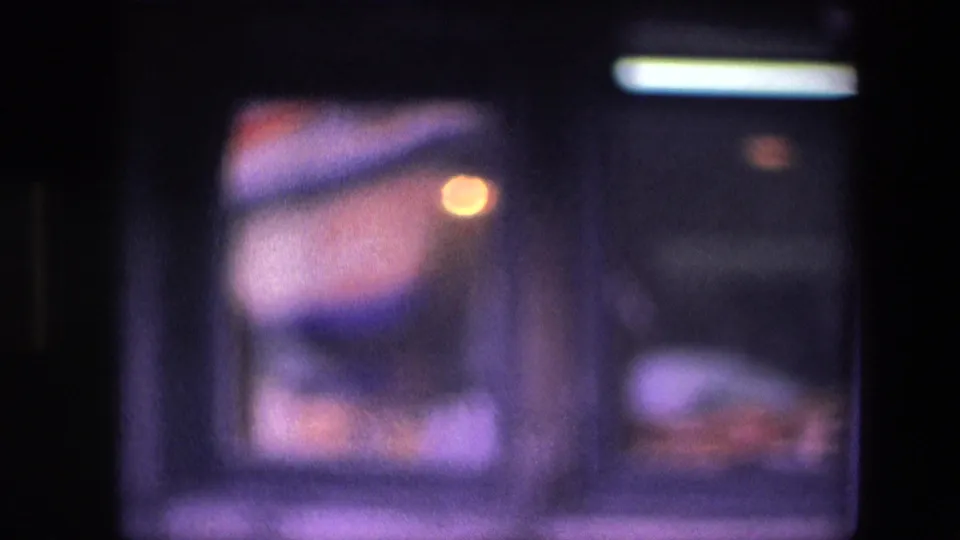 Final 1967 Amsterdam restaurant frame showing the worker lower in the window area, with dim interior light, dark framing, and soft purple-tinted film color.