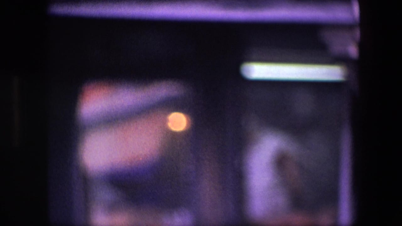 Underexposed 8mm frame with purple color cast, soft highlights, and indistinct shapes before the canal scene becomes clear.