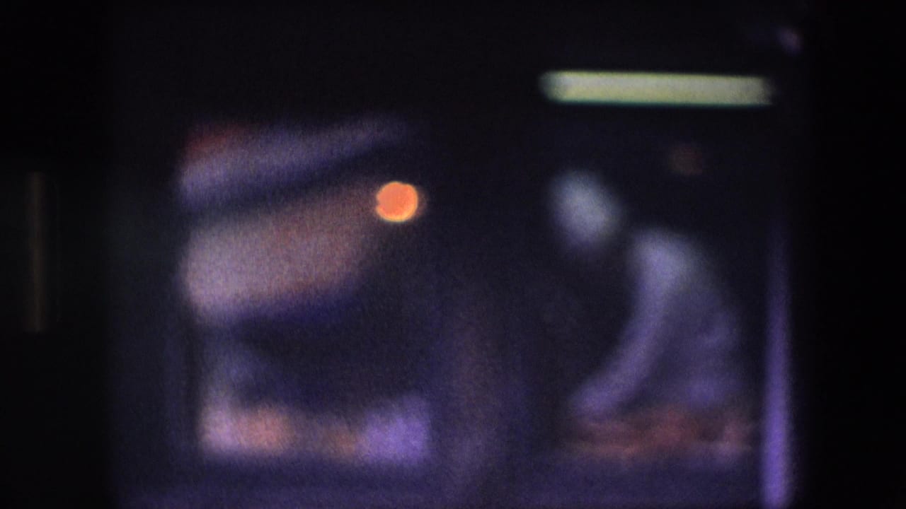 Soft, underexposed 8mm frame with a bright overhead light, purple cast, and indistinct motion before the canal view.