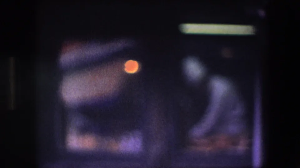 Soft, underexposed 8mm frame with a bright overhead light, purple cast, and indistinct motion before the canal view.