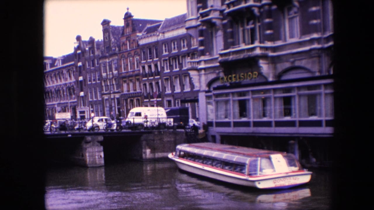 Amsterdam canal view from 1967 metadata showing a white tour boat with red trim near a bridge, parked vehicles, historic facades, and an EXCELSIOR sign.