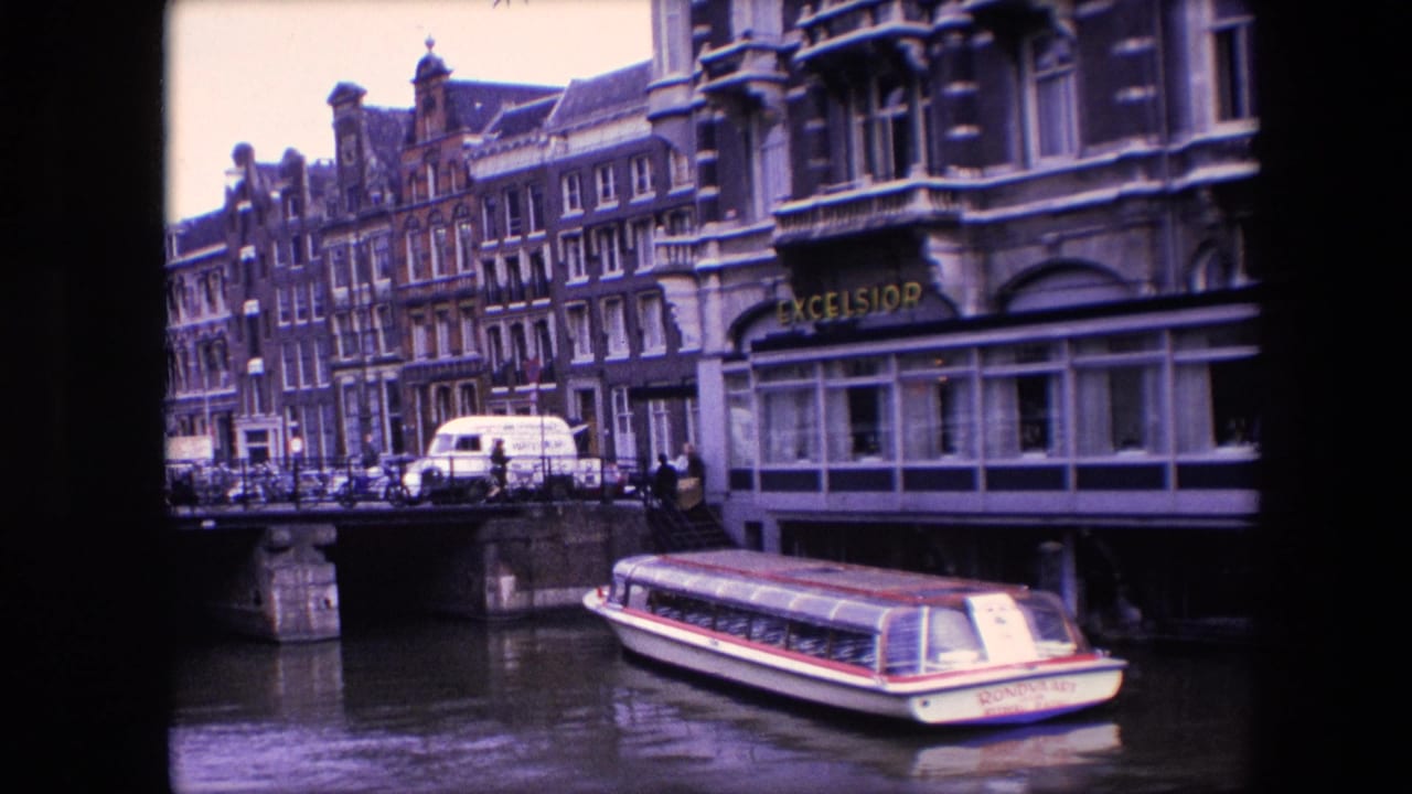 Amsterdam canal scene from 1967 showing a tour boat moving past a bridge, with a white van, pedestrians, bicycles or railings, and narrow multi-story buildings in the background.