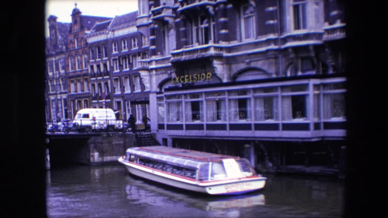 Final 1967 Amsterdam canal frame showing the tour boat lower in the frame, a stone bridge with vehicles and pedestrians, water reflections, and the EXCELSIOR building frontage.