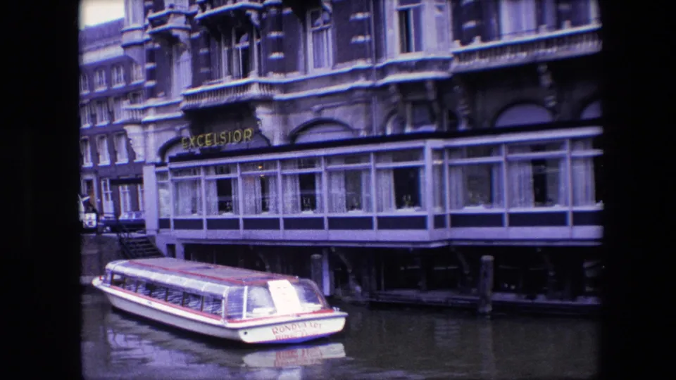 Final frame of the 1967 Amsterdam canal scene, with the white rondvaart boat at the bottom of the frame and the Excelsior hotel frontage filling the background.