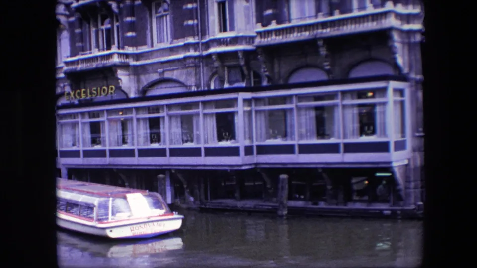 Amsterdam waterfront restaurant facade with the Excelsior sign and a moored canal boat partly framed at the lower left.