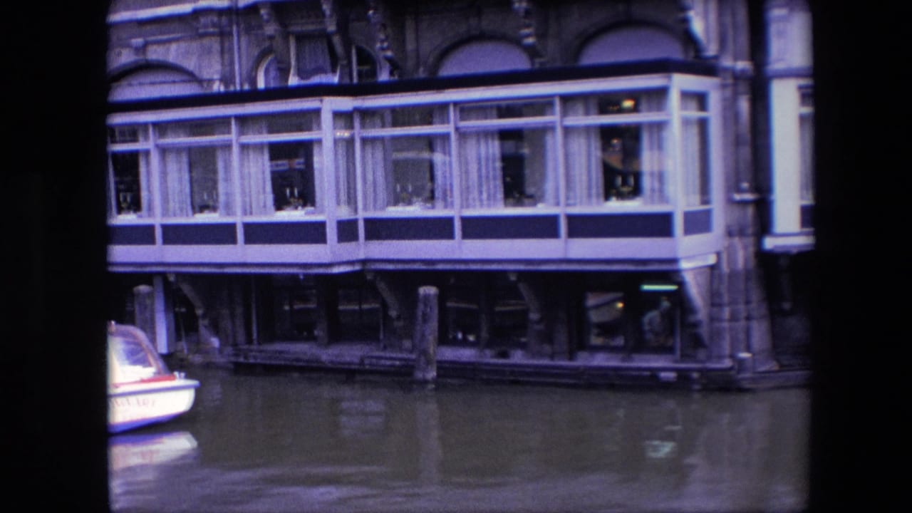 Amsterdam canal-side restaurant frontage with the glass dining terrace centered and only the edge of the canal boat remaining in frame.