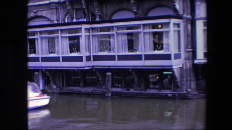 Amsterdam canal-side restaurant frontage with the glass dining terrace centered and only the edge of the canal boat remaining in frame.