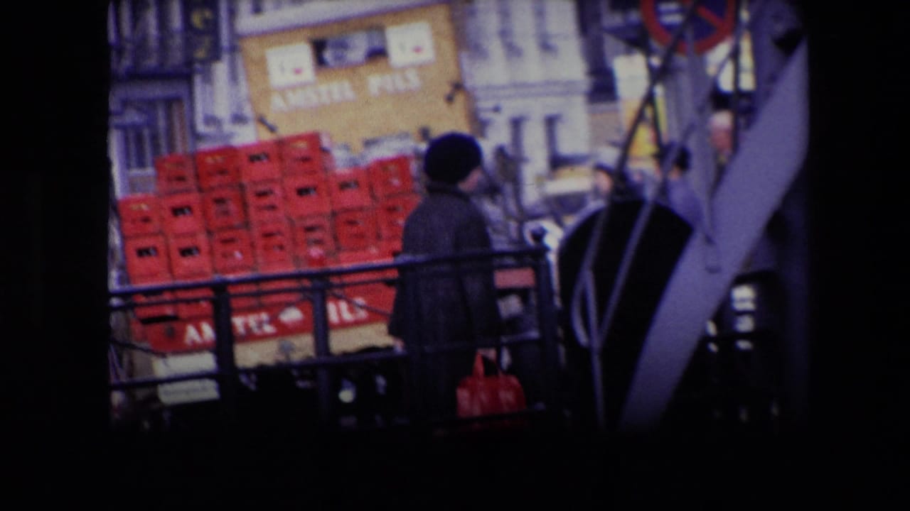 1967 Amsterdam canal-side street scene with a pedestrian carrying a red bag past stacked Amstel Pils crates and period building fronts.