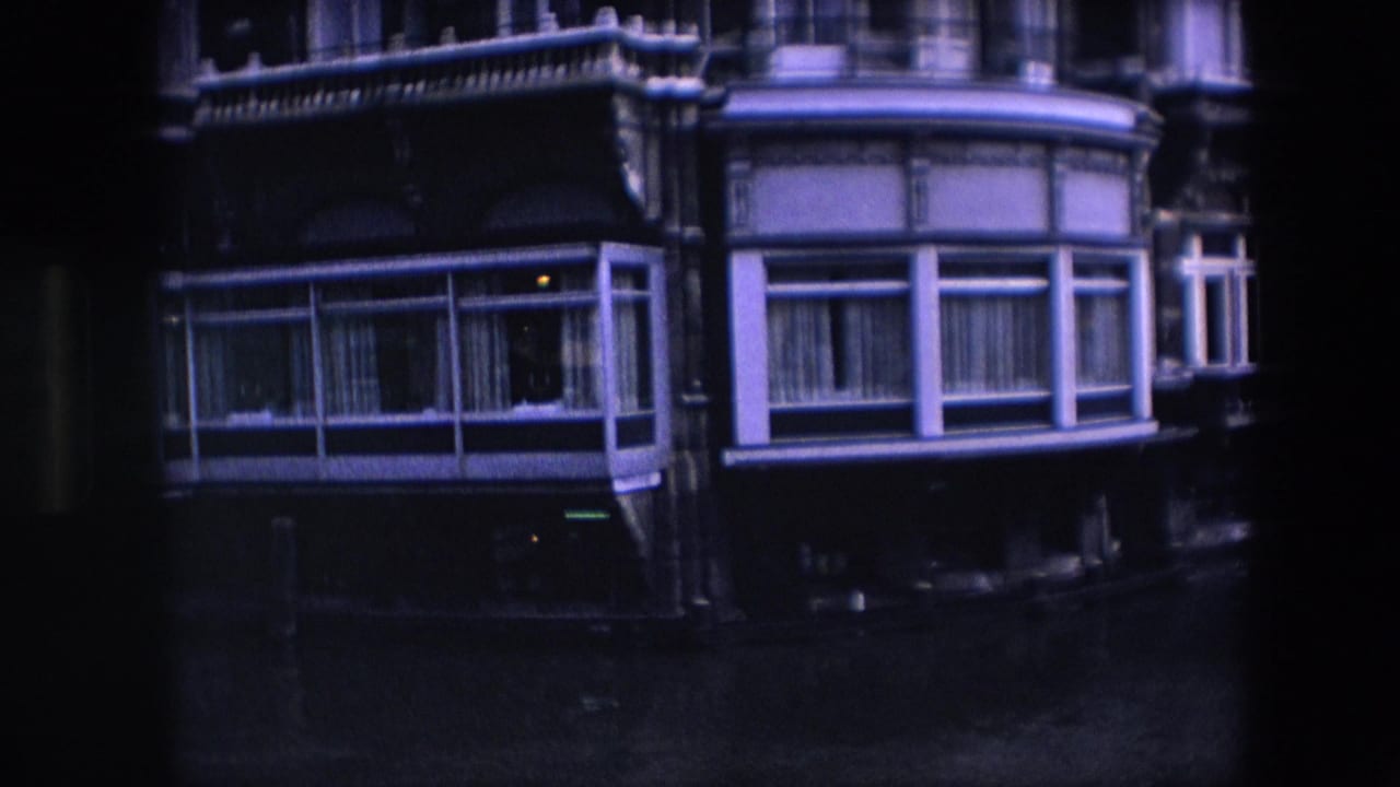 Amsterdam canal-side architecture in 1967 with projecting bay windows, curtained glass, dark stonework, and water in the foreground.