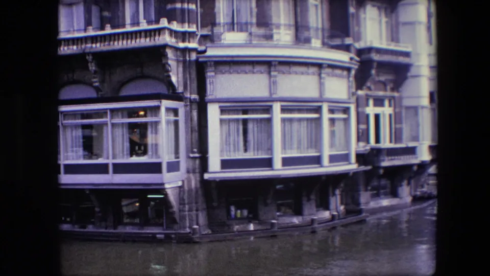 1967 Amsterdam canal architecture with enclosed bay windows, curtained upper rooms, balcony details, and dark canal water along the building edge.