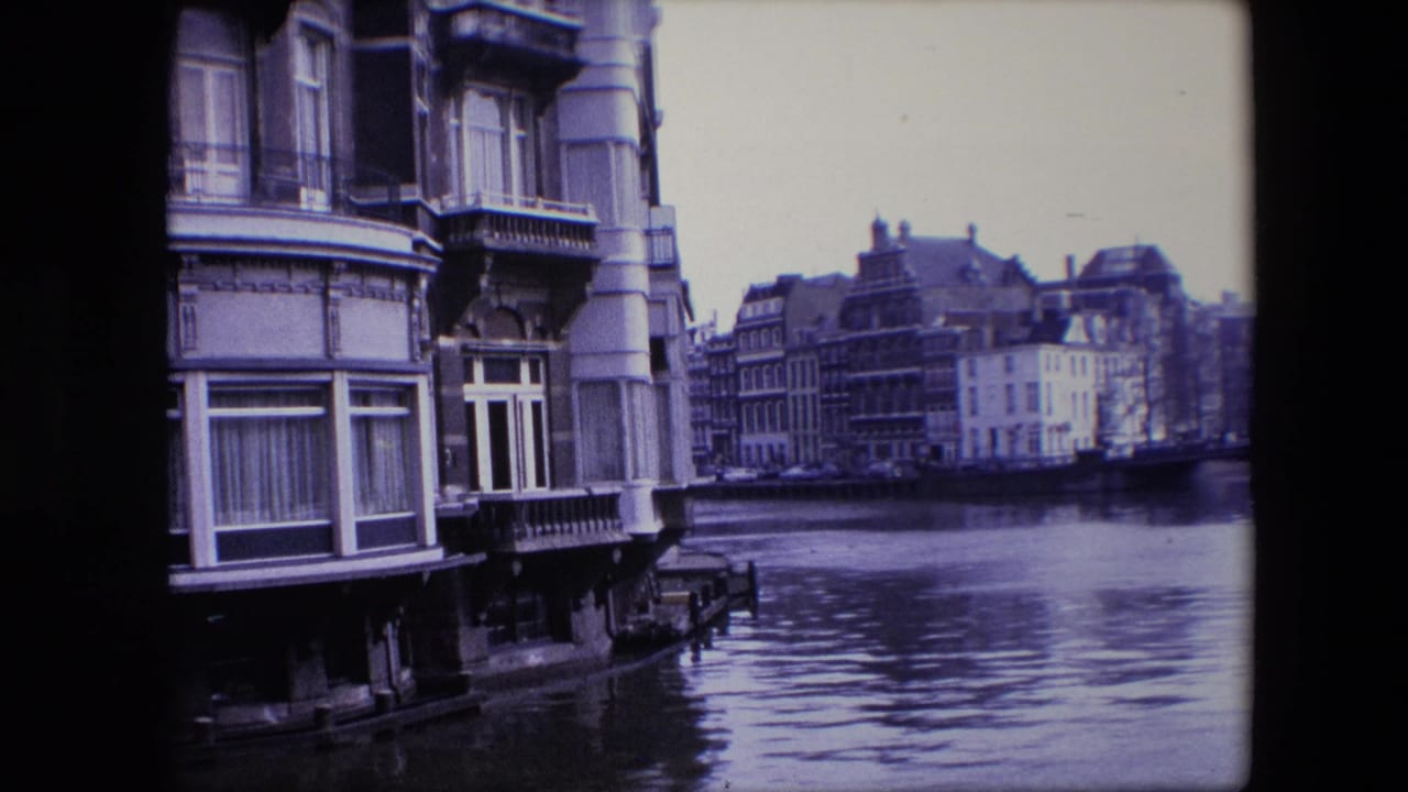 1967 Amsterdam canal view with ornate waterfront buildings, tall windows, decorative columns, and reflections across the water.