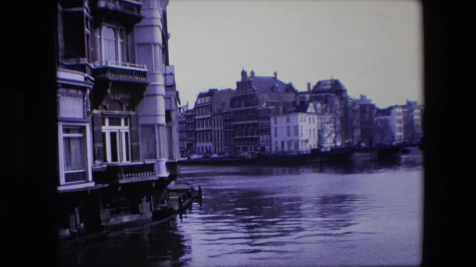 Amsterdam canal frontage in 1967, showing older multi-story buildings, a close facade at left, and calm water in the foreground.