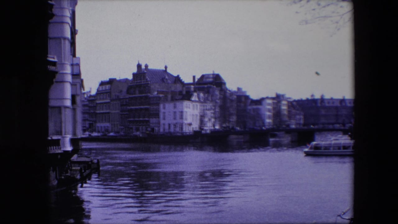 1967 Amsterdam canal view with historic buildings across the water and a small boat passing near the right side of the frame.