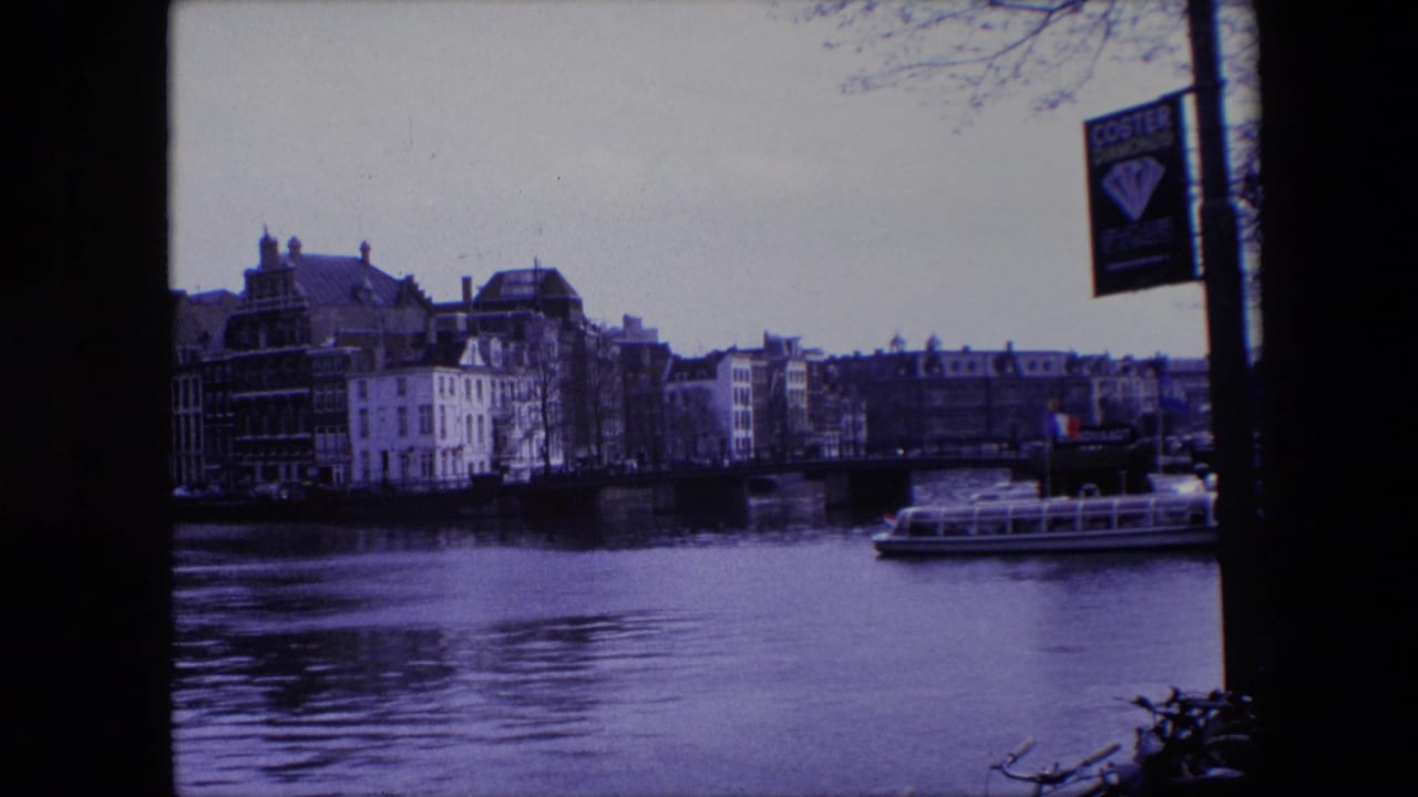 1967 Amsterdam 8mm frame with a purple cast, showing a canal, bridge, waterfront buildings, a tour boat passing along the right side, and a Coster Diamonds sign on a pole.
